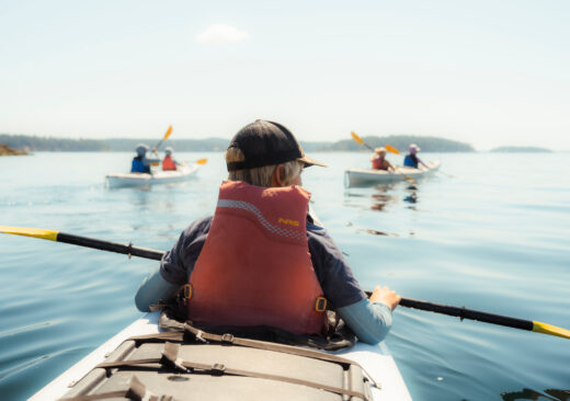 A group of kayakers paddling on calm water with a child in the foreground wearing a life jacket.