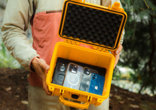 A yellow waterproof case holding four smartphones, including various models and colors.